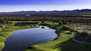 A golf course with a pond, green fairways, sand bunkers, and distant mountains. - Avi Resort & Casino (Laughlin)