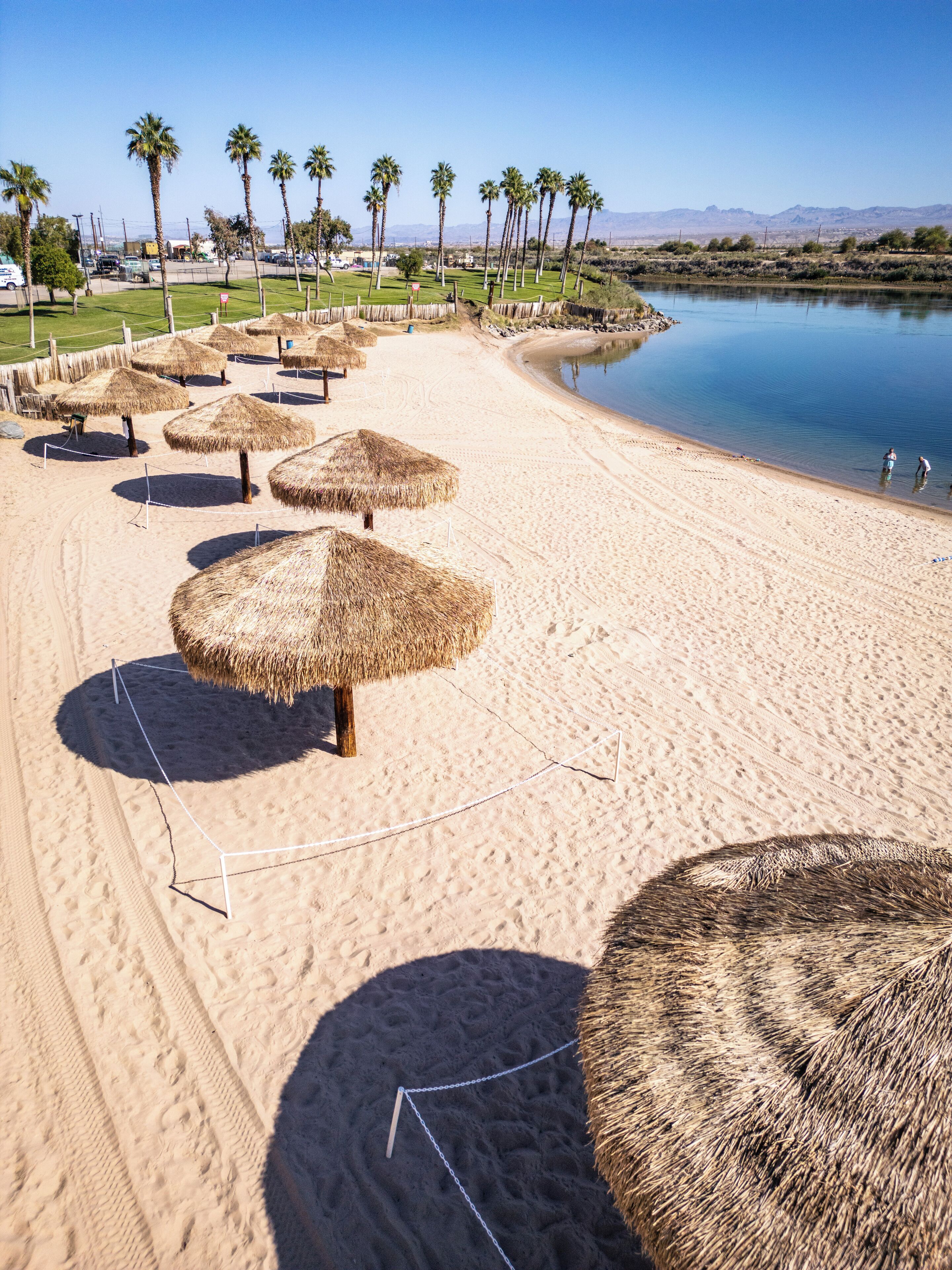 Une plage avec des parasols en chaume, des palmiers et une étendue d’eau calme.