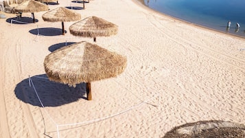 Een strand met rieten parasols, palmbomen en een kalm waterlichaam.