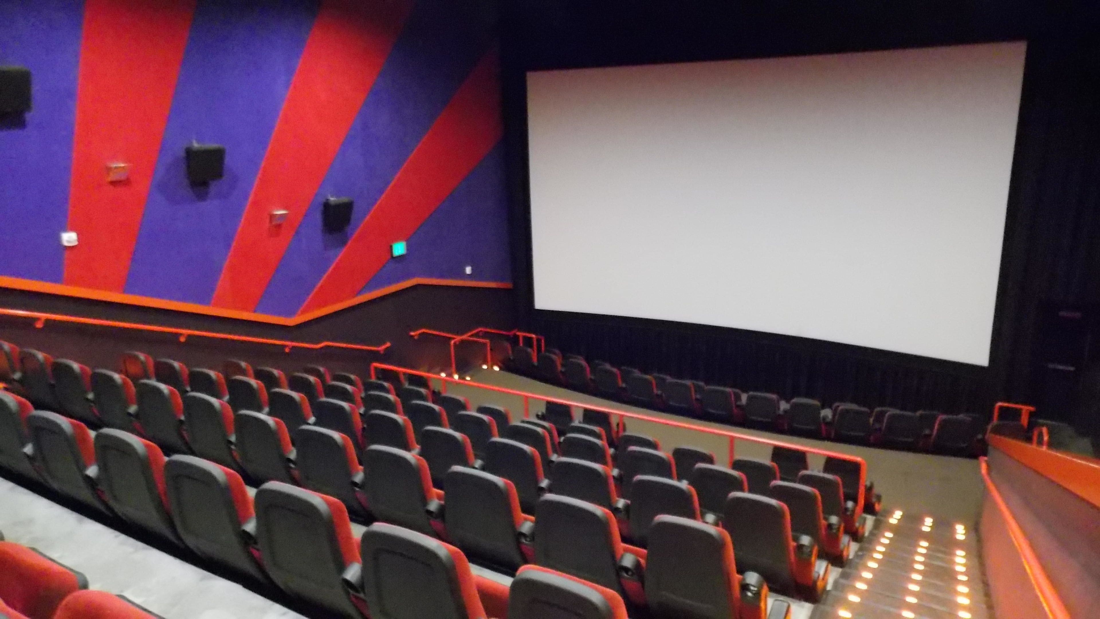 An empty movie theater with rows of red and black seats, a large screen, and a dark interior.