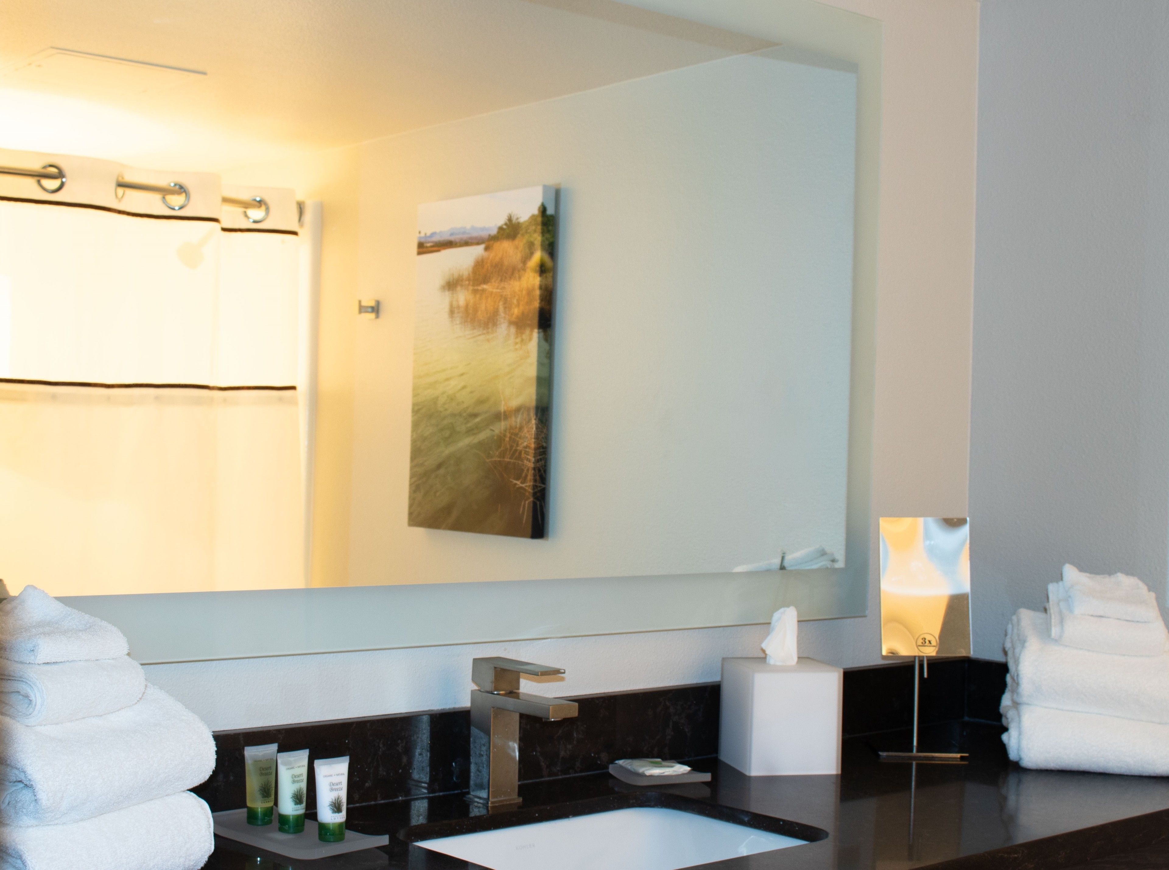 A bathroom with a large mirror, a sink, a towel rack, and toiletries.