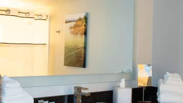 A bathroom with a large mirror, a sink, a towel rack, and toiletries.