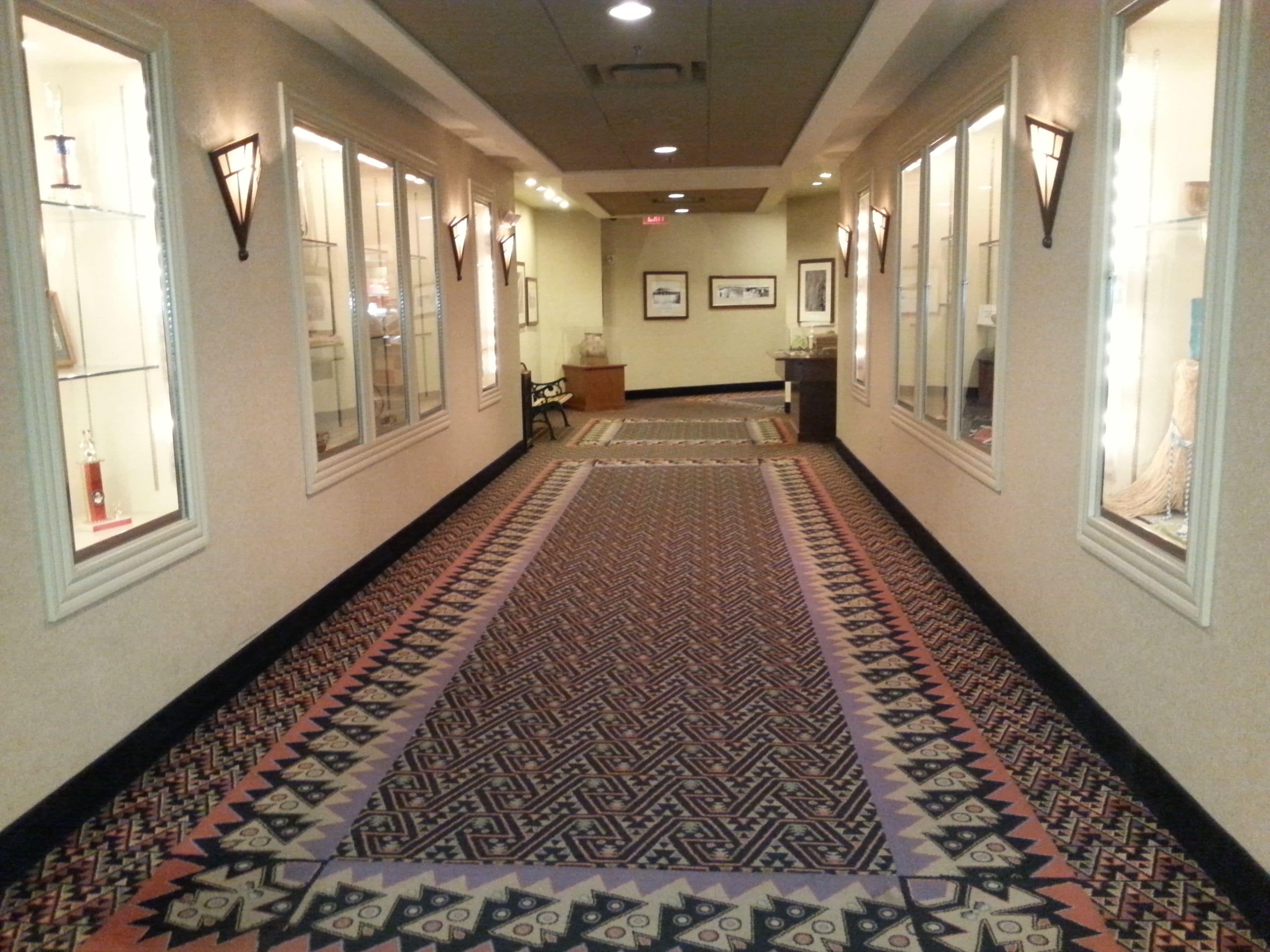 A hallway with patterned carpet, framed artwork on the walls, and a bench in the center.