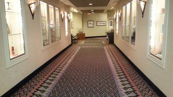 A hallway with patterned carpet, framed artwork on the walls, and a bench in the center.