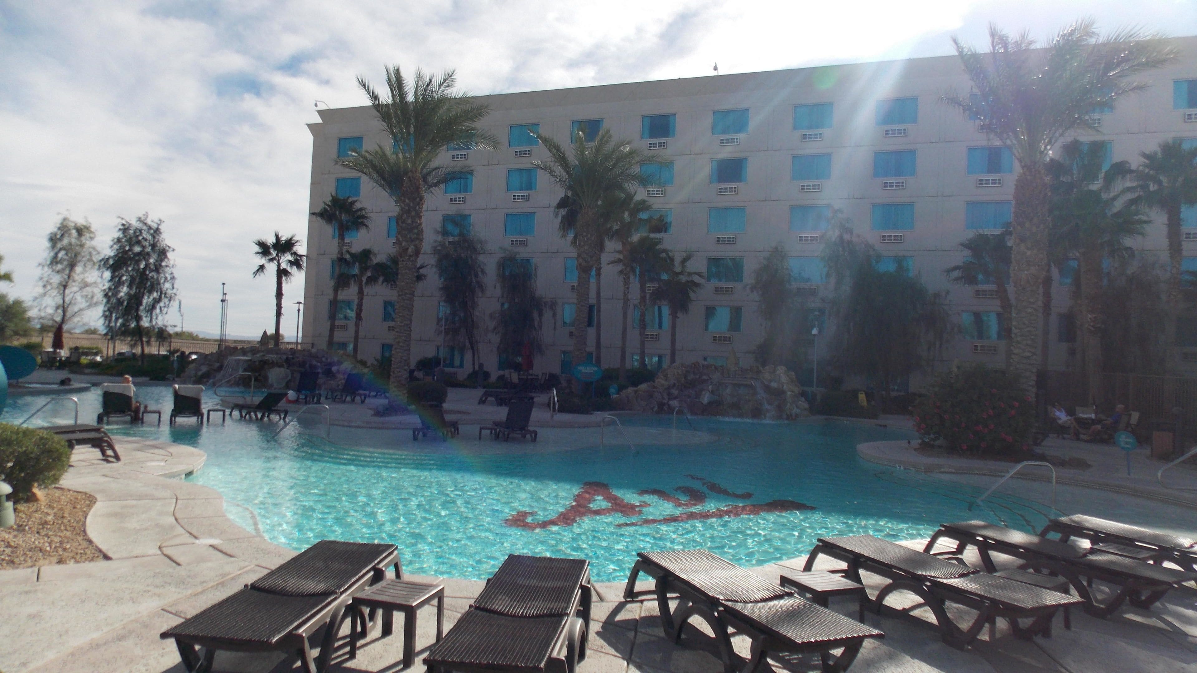 Ein Hotelpoolbereich mit Liegestühlen und einem großen Gebäude im Hintergrund.