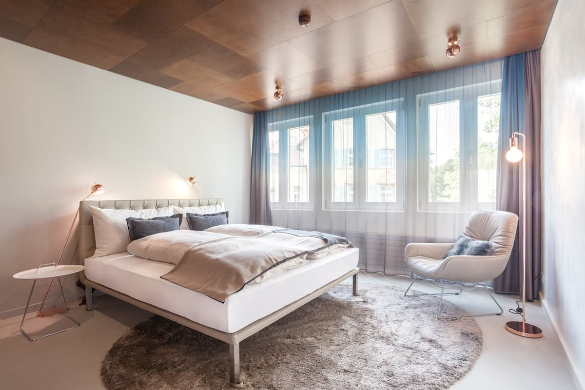 A modern bedroom with a large bed, a side table, a chair, and a floor lamp.