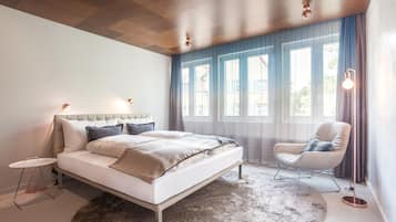 A modern bedroom with a large bed, a side table, a chair, and a floor lamp.
