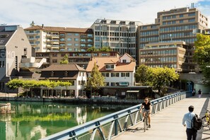 A bridge with a metal railing, a river, and buildings in the background. - EMA House Hotel Suites (Zürich)