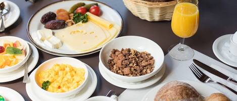 Une table dressée pour le petit-déjeuner, avec différents plats, notamment des œufs, de la viande et des viennoiseries.