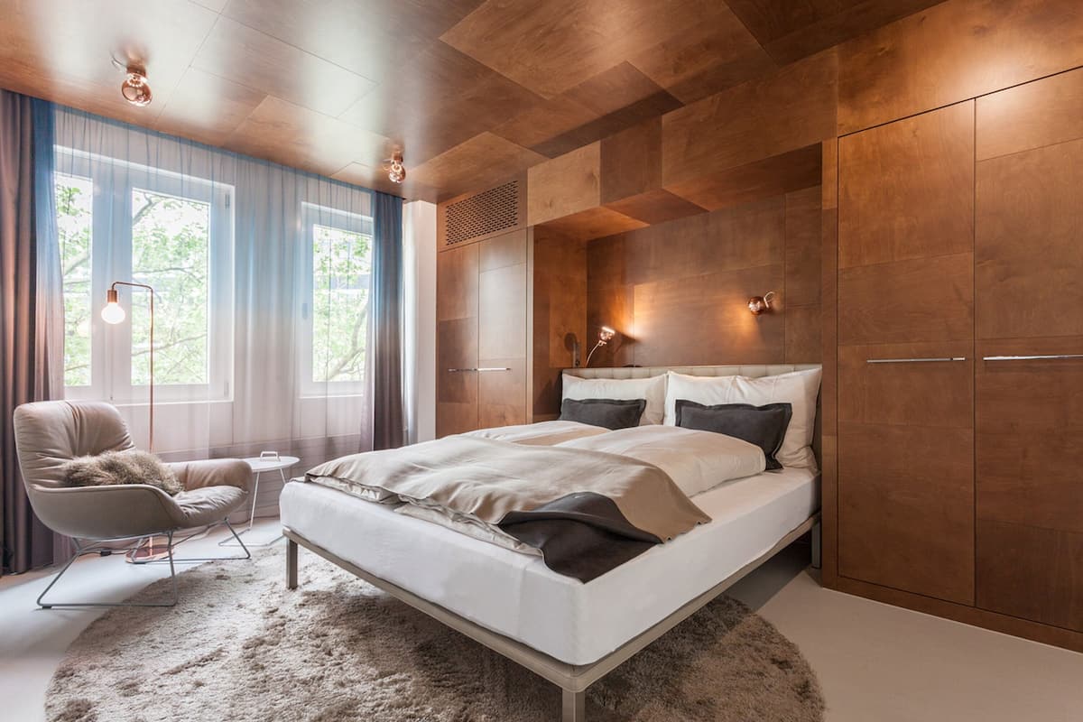 A modern bedroom with a large bed, a chair, a small table, and a wardrobe.