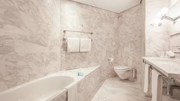 A modern bathroom with a marble wall, a bathtub, a toilet, and a sink.