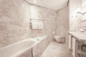 A modern bathroom with a marble wall, a bathtub, a toilet, and a sink. - EMA House Hotel Suites (Zürich)
