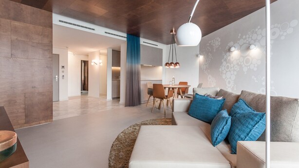 Una sala de estar moderna con sofá, cojines azules, un comedor con sillas y una cocina al fondo.