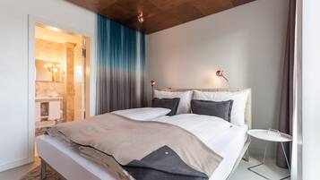 A modern bedroom with a large bed, a bedside table, a mirror, and a view of the bathroom.