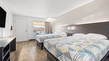 Habitación de hotel con dos camas, un escritorio, una silla, una ventana con cortinas y vistas a edificios.