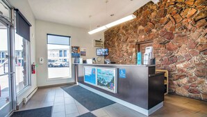 Un área de recepción con pared de piedra, mostrador de recepción, pantalla digital y vistas al exterior.