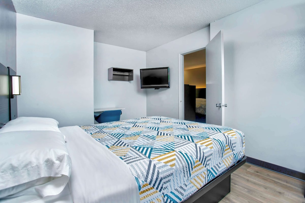 A modern hotel room with a neatly made bed, a flat-screen TV mounted on the wall, and a door leading to a bathroom.