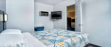 Habitación de hotel moderna con una cama bien hecha, un televisor de pantalla plana en la pared y una puerta que conduce a un baño.