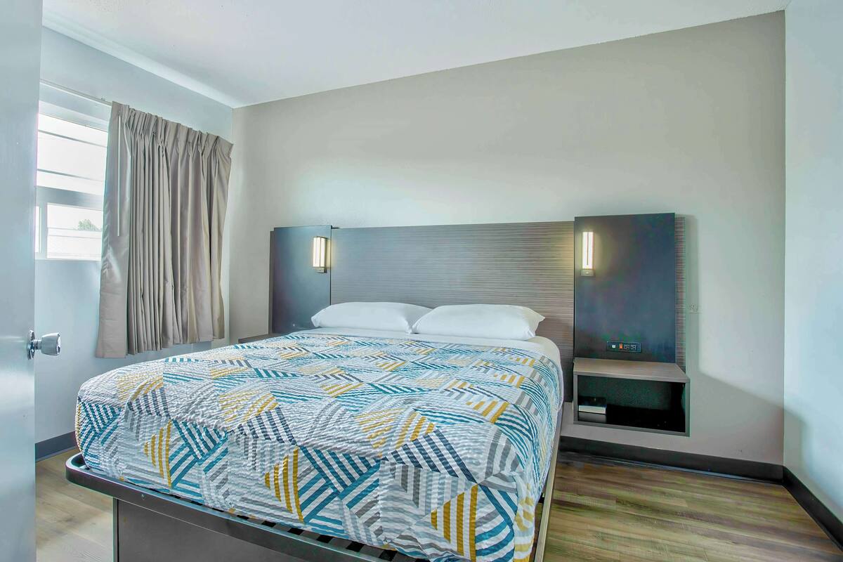 A modern hotel room with a bed, a nightstand, and a wall-mounted TV.