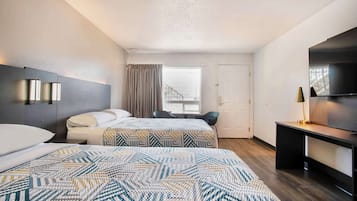 A hotel room with two beds, a desk, a TV, and a window with curtains.
