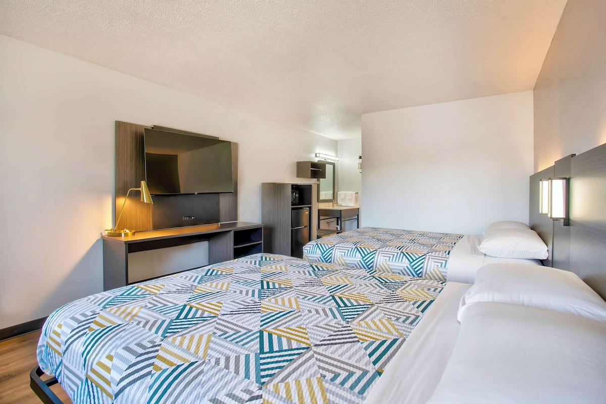 A hotel room with two beds, a desk, a mirror, and a TV.