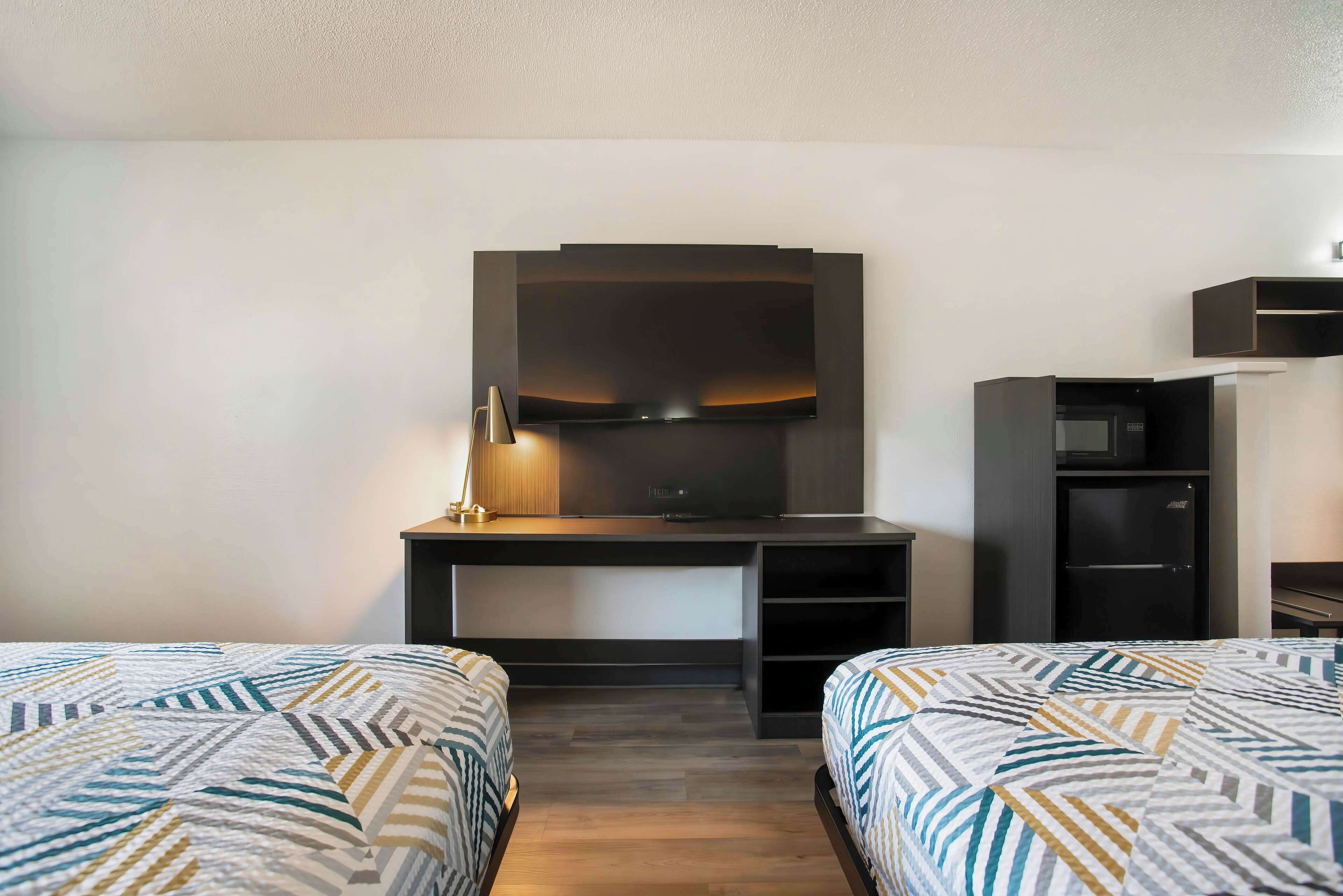 A hotel room with two beds, a desk with a flat-screen TV, a microwave, and a small refrigerator.