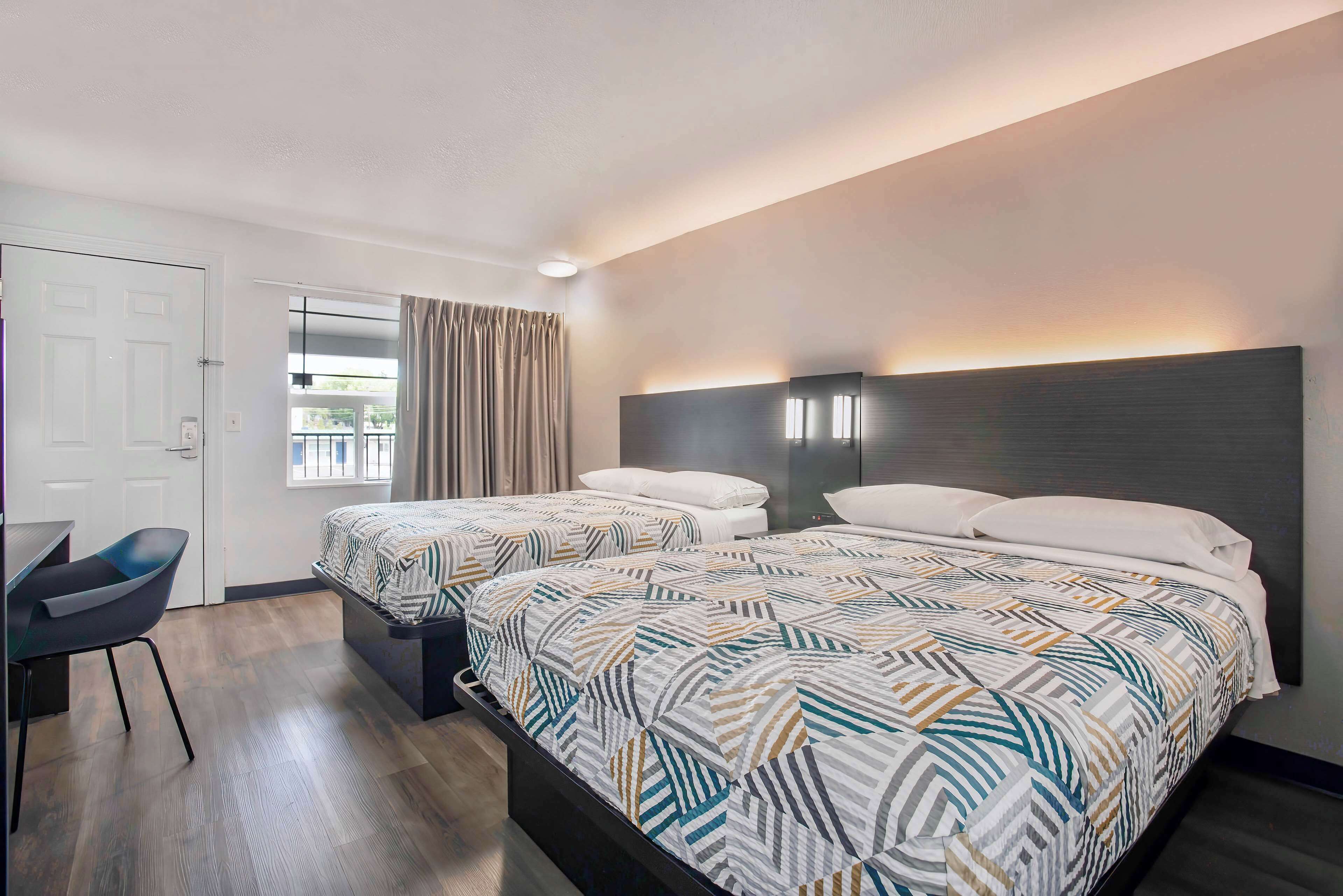 A hotel room with two beds, a desk, and a chair.