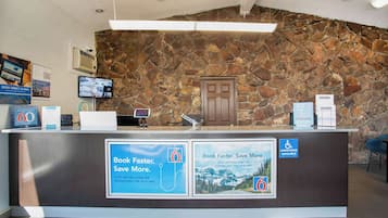 Un mostrador de recepción con un fondo de pared de piedra, una pantalla digital y carteles promocionales.