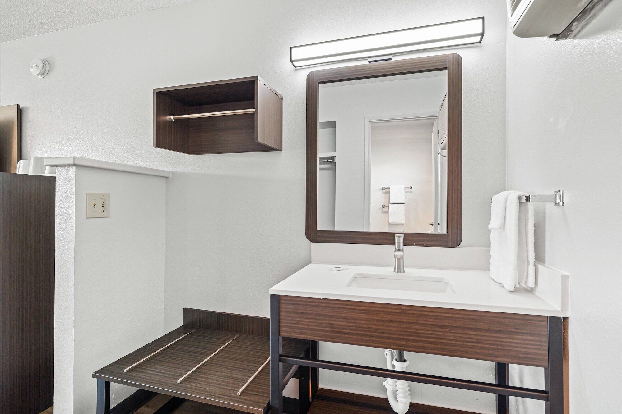Un baño moderno con tocador de madera, un espejo, toallero y una pequeña estantería.