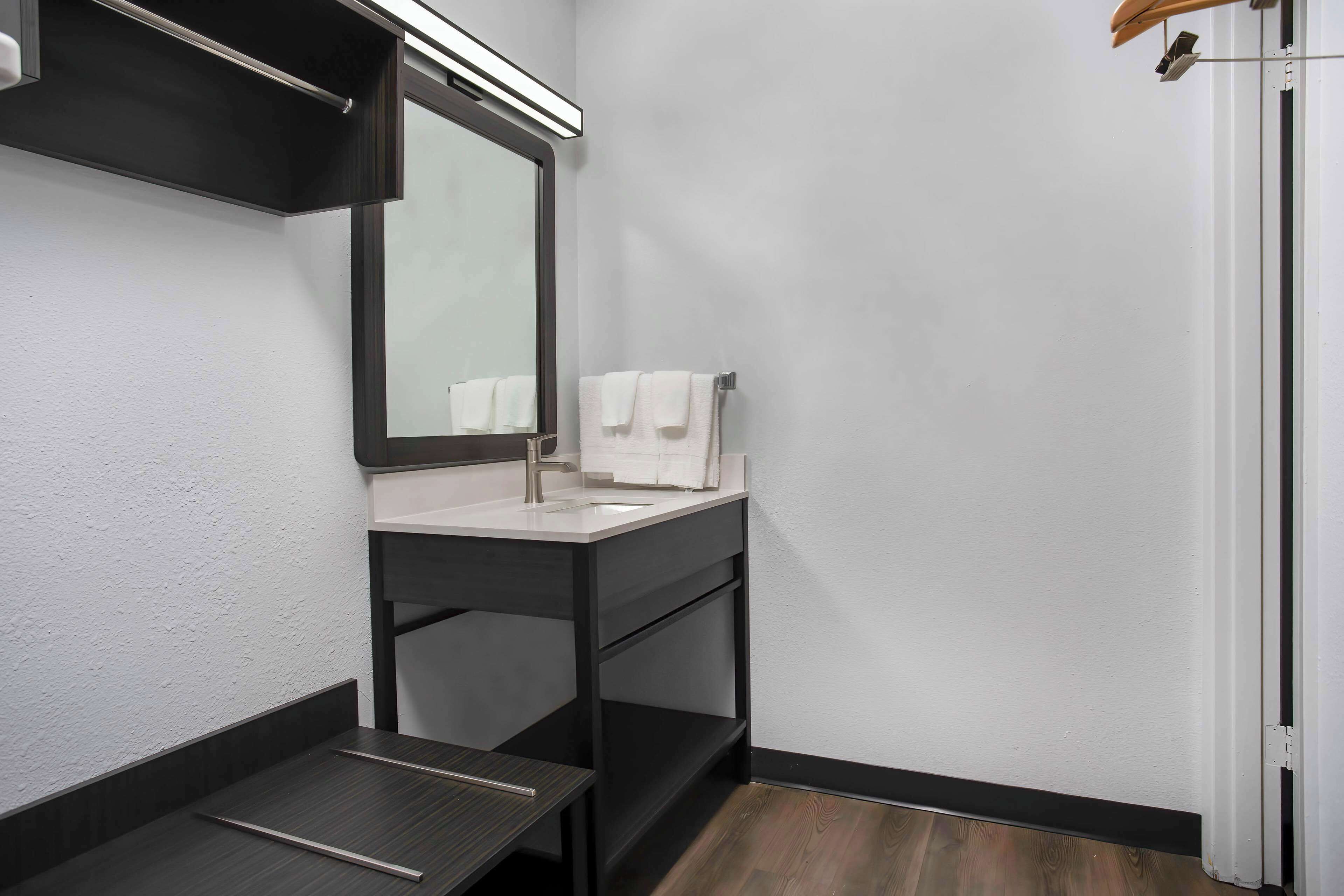 A modern bathroom with a dark vanity, a mirror, and a white sink.