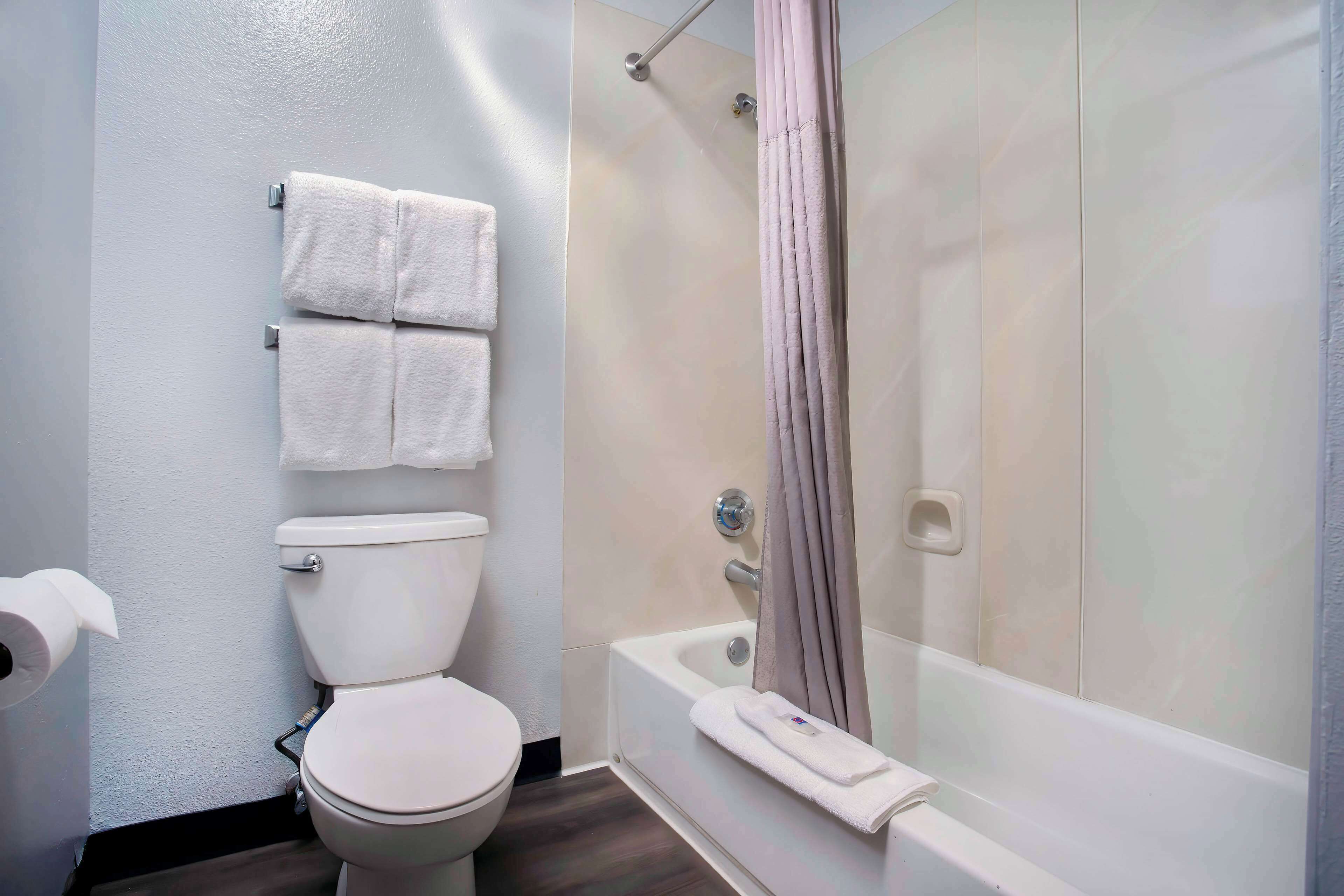 A bathroom with a toilet, a shower with a curtain, and a bathtub with a towel.