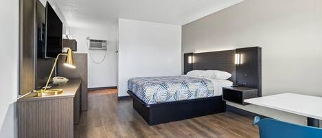 A modern hotel room with a bed, desk, chair, and a TV.