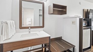 A bathroom with a white sink, a mirror, a towel rack, a wooden vanity, a small wooden shelf, and a refrigerator. - Motel 6 Bend, OR (Bend)