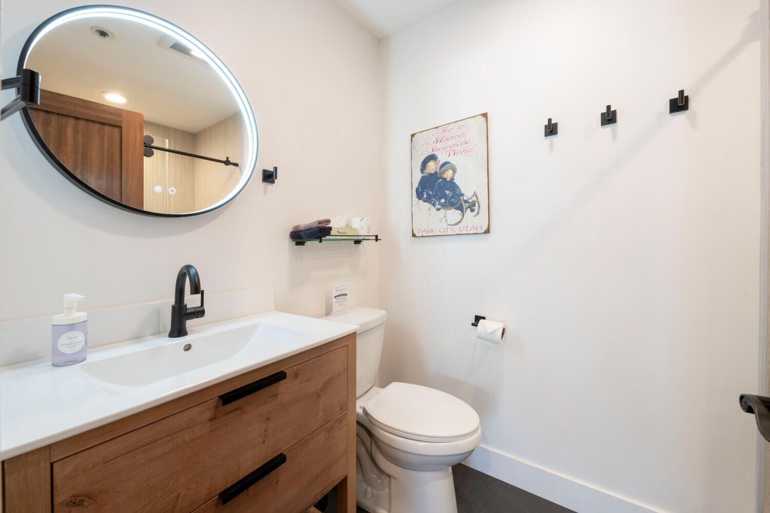 A bathroom with a round mirror, a sink with a faucet, a toilet, and a small shelf with toiletries.