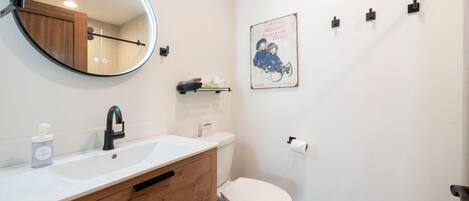A bathroom with a round mirror, a sink with a faucet, a toilet, and a small shelf with toiletries.