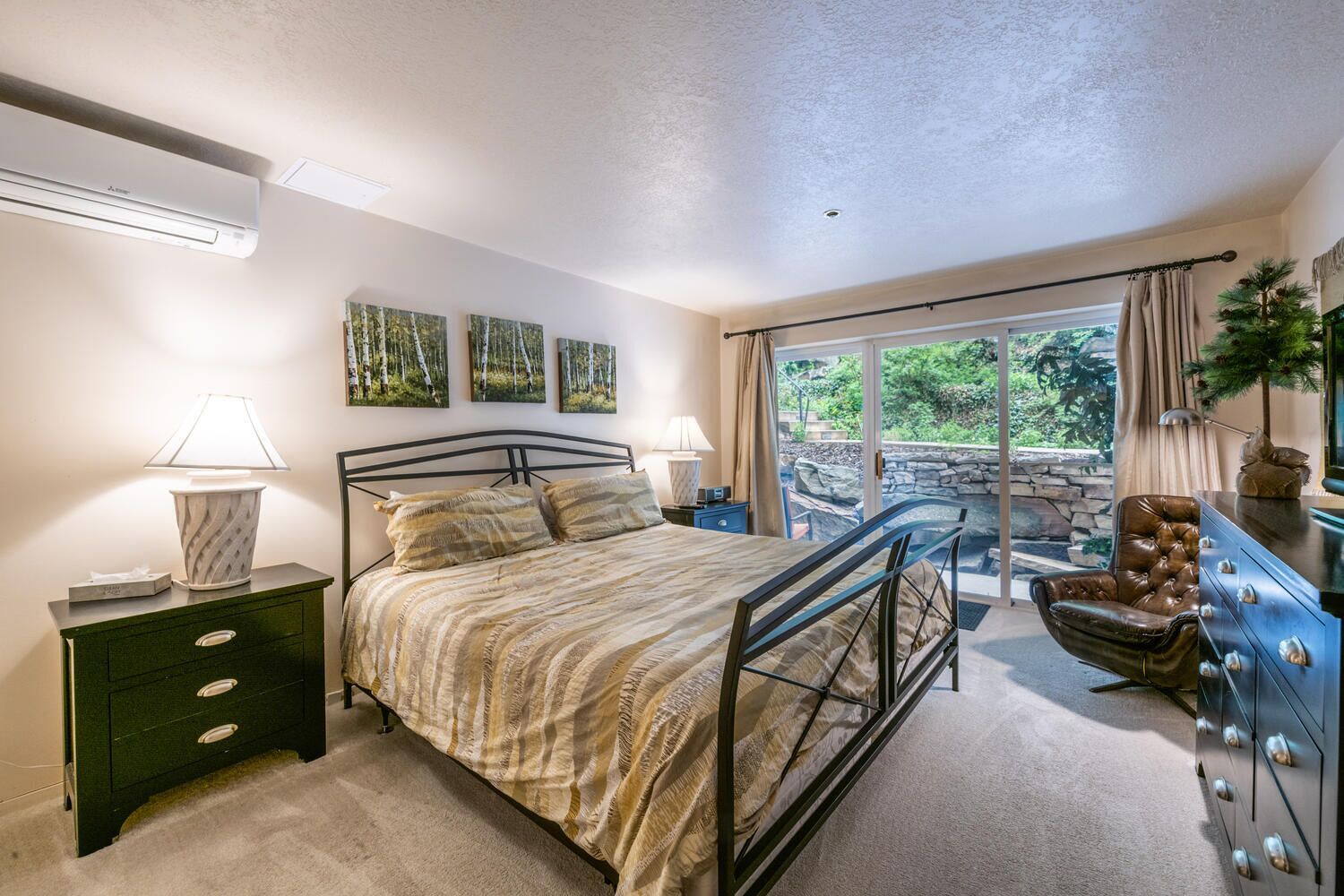 Une chambre à coucher comprenant un lit, des tables de chevet, une commode et donnant sur l’extérieur.