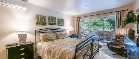 Une chambre à coucher comprenant un lit, des tables de chevet, une commode et donnant sur l’extérieur.