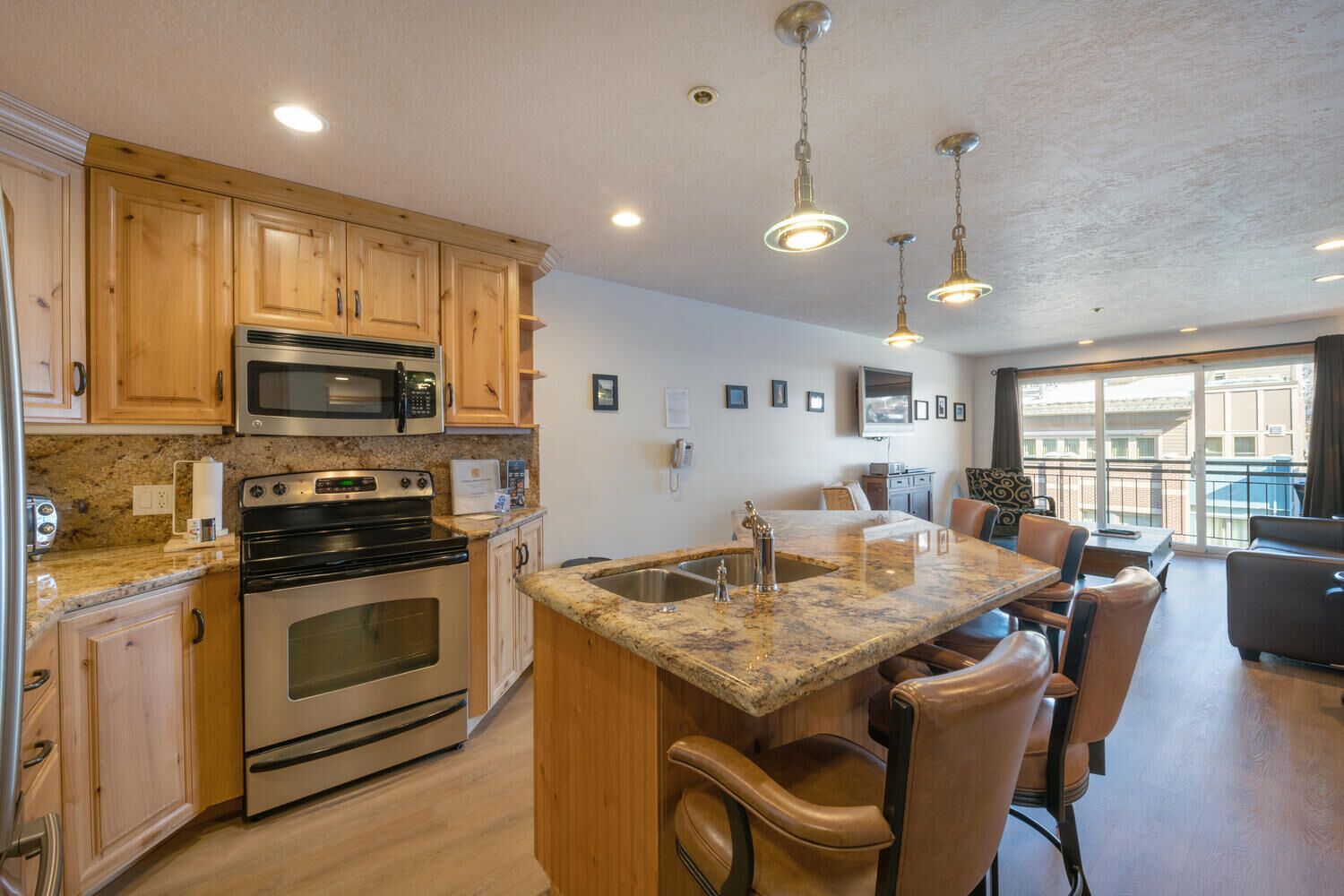 A modern kitchen with granite countertops, stainless steel appliances, wooden cabinets, and a central island with bar stools.