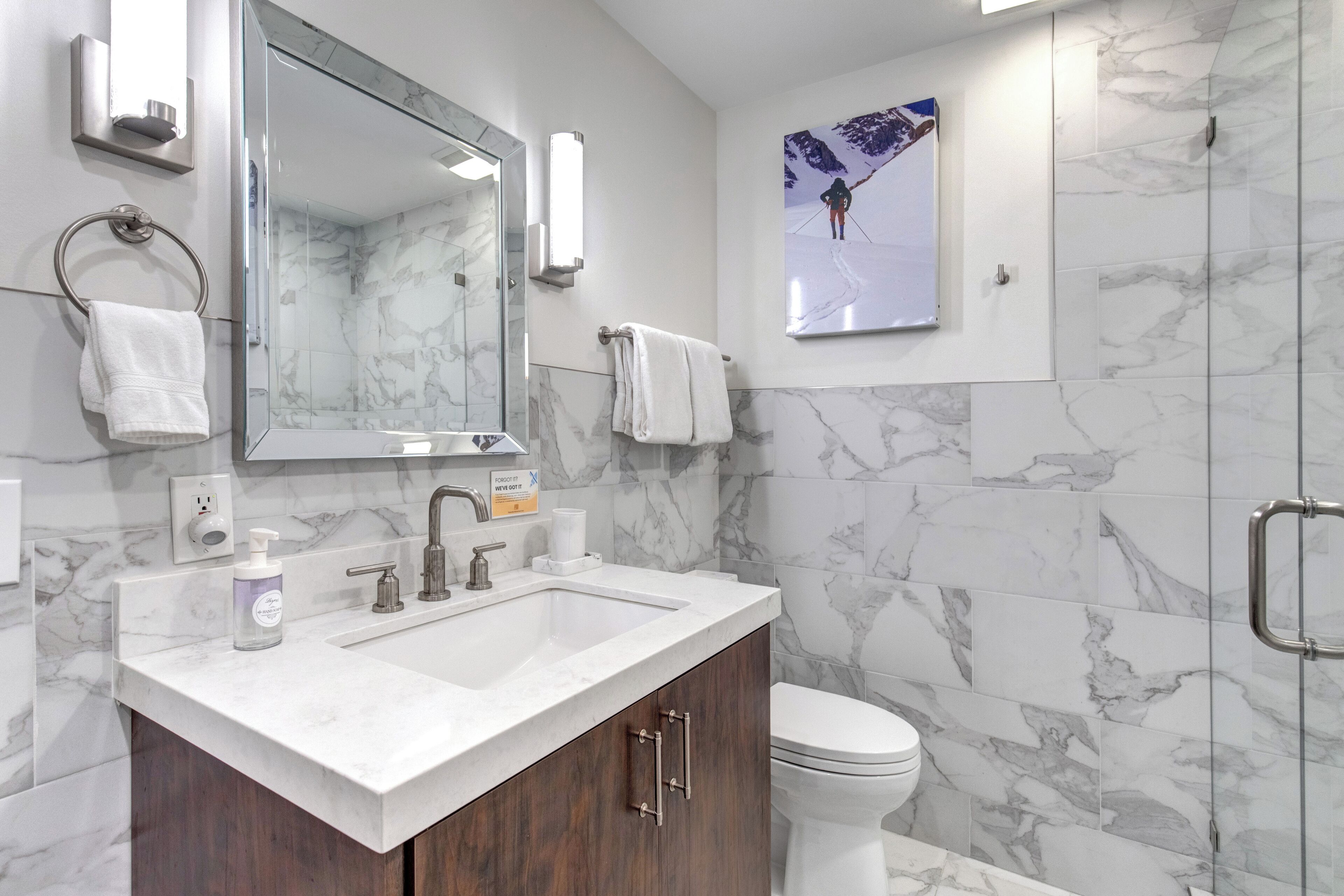 A modern bathroom with a marble sink, a large mirror, a toilet, and a shower enclosure.