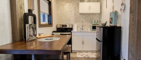 A compact kitchen with a wooden table, built-in appliances, and a small window with blinds.