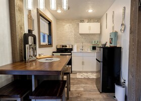Une cuisine compacte avec une table en bois, des appareils électroménagers intégrés et une petite fenêtre avec des stores.
