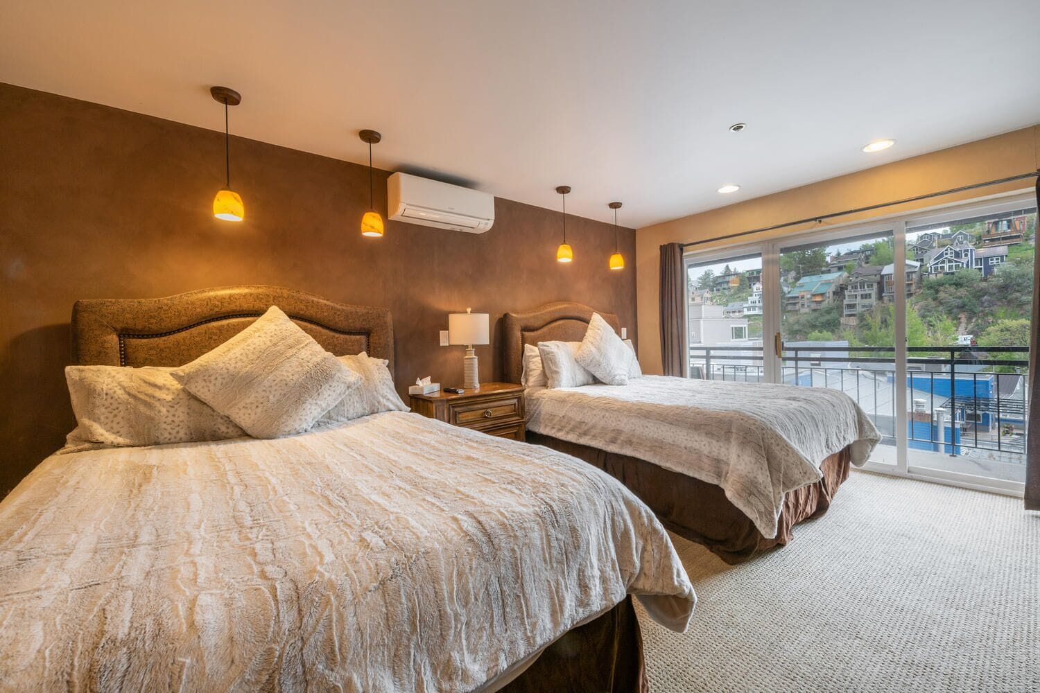 Une chambre d’hôtel avec deux lits, une table de chevet, une lampe et une vue sur la ville grâce à de grandes fenêtres.