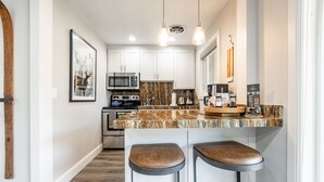 Una cocina moderna con armarios blancos, encimera de granito, microondas integrado, estufa y dos taburetes de bar.
