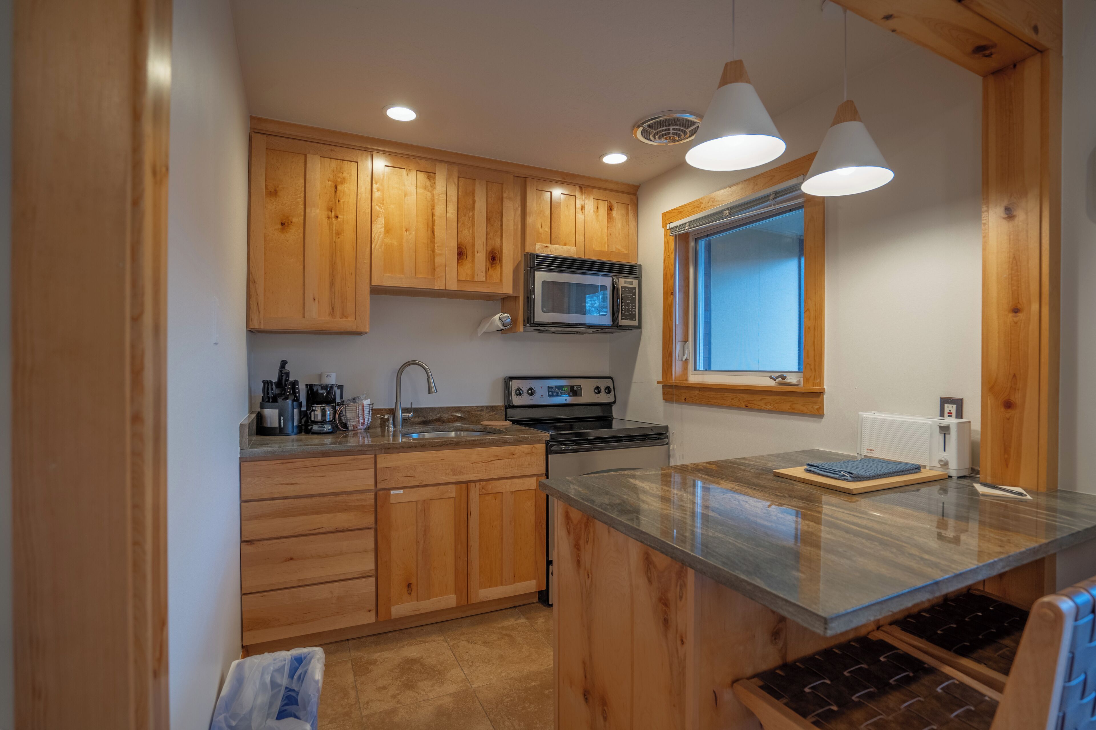 Una cocina con armarios de madera, microondas, estufa y ventana.