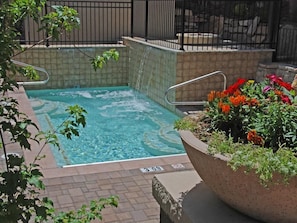 A hot tub with a tiled surround and a planter with colorful flowers.