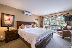 A hotel room with a large bed, a sitting area with a chair, a TV, and a balcony with a view of the city.