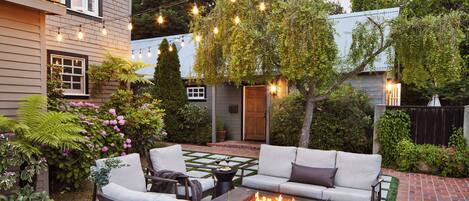 Un patio con una chimenea, mobiliario exterior e iluminación con luces colgantes.