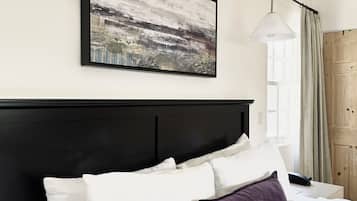 A hotel room with a large bed, white bedding, a black headboard, a framed abstract painting, and two pendant lights.