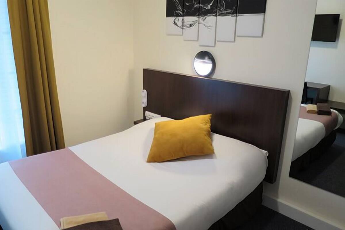 A hotel room with a bed, a nightstand, a mirror, and a window with curtains.