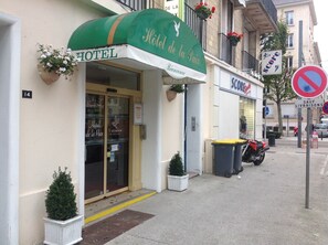 A hotel entrance with a green awning, a sign reading "Hotel de la Paix," and a "Welcome" sign. There are potted plants and a "WiFi" sign on the door. - Hotel de la Paix (Caen)